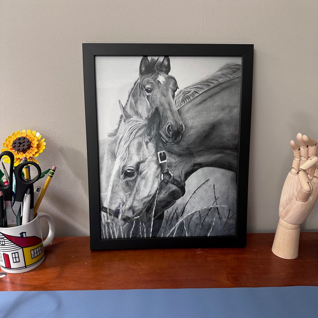 Framed print of graphite drawing of a mare and her foal. Close up of Mare eating grass and foal with head over mare's ears